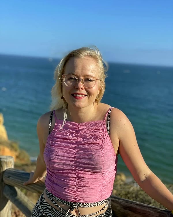 Aino smiling by the sea in a pink top