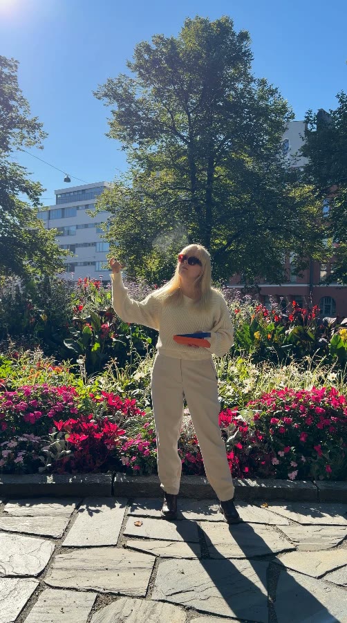 Aino in a park full of flowers, holding a perfume box