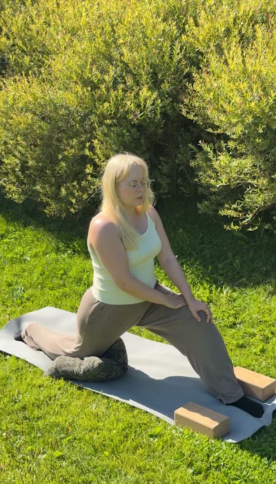 Aino in a low lunge on a yoga mat in the garden